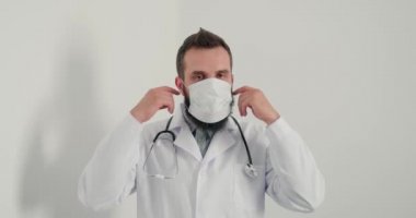 Erkek doktor tıbbi maske takıp kameraya bakıp gülümsüyor. Klinikte internet üzerinden steteskop danışmanlığı yapan sakallı bir pratisyen.