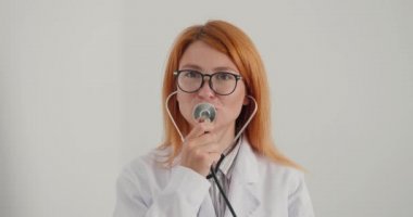 Kadın doktor klinikte eğleniyor. Genç terapist şaka yapmak için steteskobu mikrofon olarak kullanıyor. Neşeli bayan iş yerinde şarkı söyleyip dans ederken eğleniyor.