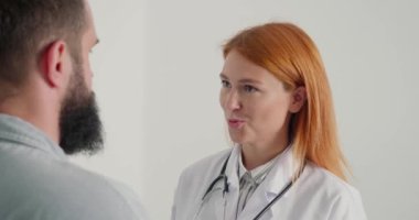 Kızıl saçlı kadın doktor hastasına danışmanlık yapıyor. Doktor beyaz önlükle çalışır ve yetişkin bir adama tavsiye verir. Bayanın her zamanki çalışma günü.