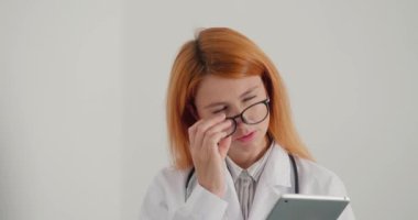 Kızıl saçlı kadın doktor tablet üzerinde çalışıyor. Terapist hastalara çevrimiçi danışmanlık yapıyor. Kadın gözlüklerini çıkardı ve dikkatli bir şekilde şüpheli bir teşhis koydu.