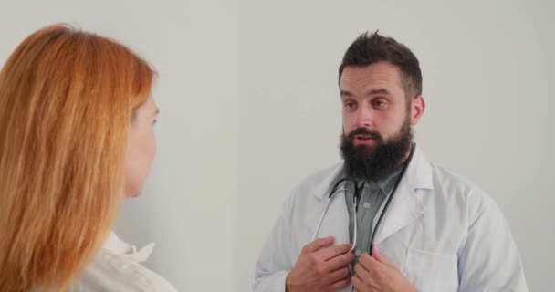 男医生笑着询问女病人在办公室的预约情况 头戴白衣 头戴听诊器的医生为成年女性特写提供建议 — 图库视频影像