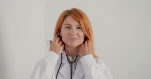 Vrouwelijke Dokter Glimlacht Legt Stethoscoop Rond Nek Kijkend Camera Roodharige — Stockvideo