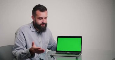Yönetici, Cromakey Green ekranında yeni ürünü gösteriyor. Sakallı adam ofisteki sandalyede oturuyor.