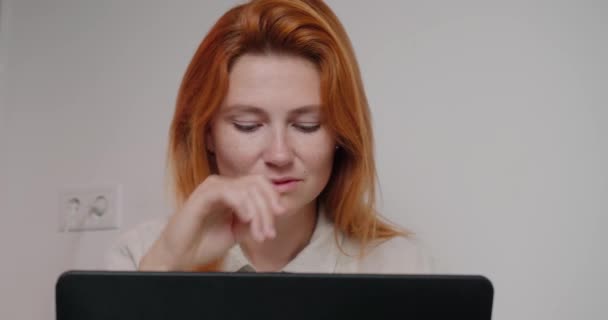 ジンジャーヘアの成功した女性は ノートパソコンで作業机の上に座っています 集中した女性はプロジェクトのクローズアップで考える現代的なデバイスの画面を見ています — ストック動画