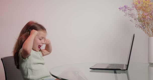 小さな女の子は 現代のラップトップを介してビデオ通話で友人に優雅さを示す笑顔 面白い子は 部屋のクローズアップで机に座っているデバイスの画面を見て — ストック動画