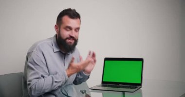 Profesyonel koç, dizüstü bilgisayardaki kromakey yeşil ekranda örnekler gösteren kod yazmaktan bahsediyor. Sakallı adam ofiste online video kursu yönetiyor.