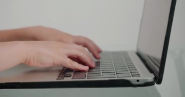 Okul çocuklarının parmakları beyaz arka plandaki cam masadaki modern cihazın klavye tuşlarına basıyor. Küçük kız dizüstü bilgisayarda mesajları yakın plan çekimde yazıyor.