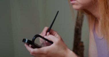 Kızıl saçlı kadının elleri çalılıklara gölge düşürüyor ve göz kapakları takıyor. Bayan sabah işe gitmeden önce bulanık arkaplanda makyaj yapar.