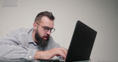 Duygusal adam işini çabuk bitirmek için klavyeye vuruyor. Gözlüklü, şaşırtıcı sakallı programcı ofisinde oturuyor ve görevini tamamlıyor.