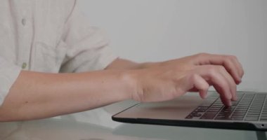Ofisteki cam masada duran kadın tipleri dizüstü bilgisayardan rapor veriyor. Bayan çalışanın elleri modern cihazın klavyesindeki tuşlara basar.