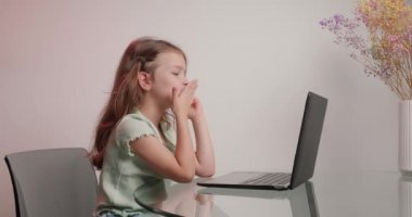 Tatlı kız bilgisayarla annesiyle canlı yayında konuşuyor. Öğrenci kız, vazoda kurumuş çiçek dallarının yanında yuvarlak cam masada oturuyor.