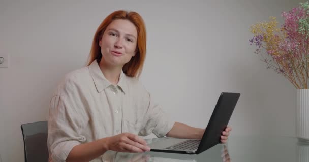 Redheadの財務コーチは例を示すためにラップトップを使用して投資について話します 若い女性は ガラスデスクでカメラにデバイスのクロマキー緑の画面をオンにします — ストック動画