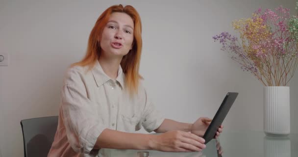 Redhead Managerは ラップトップのターンキー緑色の画面に新しいプロジェクトを表示します 笑顔の女性は花瓶のカラフルな花の近くのガラステーブルに座っている — ストック動画