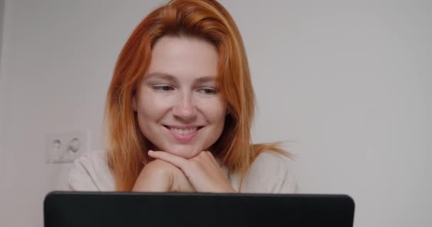 快乐的女人坐在桌旁 通过现代笔记本电脑与亲戚进行视频通话 红头发女士喜欢和白墙特写交流 — 图库视频影像