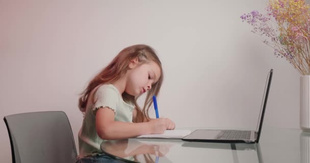 勤勉な少女は教師とのビデオ通話で練習帳に書かれた完成したタスクを示しています 小さな子供は家の机に座ってオンライン教育を受ける — ストック動画