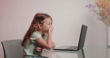 Çalışkan, sıkkın liseli kız, bilgisayar aracılığıyla öğretmeniyle video konferansında iletişim kurarak masada oturuyor. Küçük kız evde internetten eğitim görüyor.