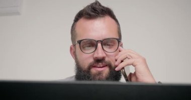 Gözlüklü bir çalışan yeni projeyi konuşmak için telefonda müdürle görüşüyor. Sakallı adam masa başında oturup ofiste bilgisayarla yakından ilgileniyor.