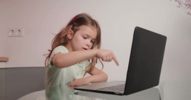 Dizüstü bilgisayarında baş parmak hareketi gösteren neşeli kız tipleri. Küçük bir okul öğrencisi evdeki modern aletleri kullanarak öğreneceği için heyecanlanıyor.