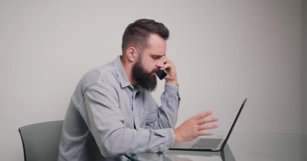 烦躁的员工与同事在电话上争吵 身穿经典衬衫 留着胡子的男人在总公司米黄色的墙上靠着桌子坐着 — 图库视频影像