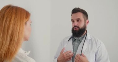 Erkek doktor klinikteki hastaya danışmanlık yapıyor. Beyaz önlüklü sakallı pratisyen, olgun kadınlara tavsiyelerde bulunur. İnsanın her zamanki çalışma günü.