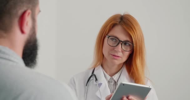 红头发女医生在治疗后会见了健康的男性病人 治疗师笑着遇见了男人 女士在办公室有正常的工作日特写镜头 — 图库视频影像