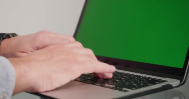 Bilinmeyen adam rapor saatini kontrol ediyor ve dizüstü bilgisayarını kromakey yeşil ekranla kapatıyor. Freelancer 'ın elleri aygıt klavyesindeki tuşlara basar