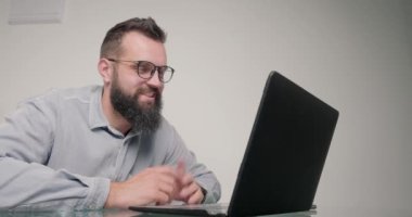 Gözlüklü çalışan, iş arkadaşıyla bilgisayar aracılığıyla konuşuyor. Yetişkin sakallı adam ofisinde oturan arkadaşıyla iletişim kuruyor.