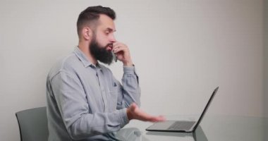 Sakallı adam laptopta çalışıyor ve telefon konuşmasını engelliyor. Adam hızlı bir konuşma için zaman ayırıyor, bilgisayarını kapatıyor ve işini bitiriyor.. 