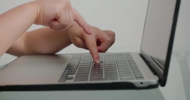 Okul çocuklarının parmakları beyaz arka plandaki cam masadaki modern cihazın klavye tuşlarına basıyor. Küçük kız dizüstü bilgisayarda mesajları yakın plan çekimde yazıyor.