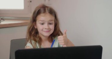 Küçük kız, el hareketi yazısını egzersiz kitabında kalemle gösteriyor. Odaklanma odasında dizüstü bilgisayarla öğretmenle video konferansında öğrenci
