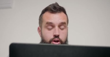 Erkek tasarımcı müşteriyle telefon yeşil ekranında görüntüyü dizüstü bilgisayarla konuşur. Sakallı çalışan ofiste oturmuş yeni anlaşmayı tartışıyor.