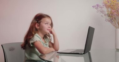 Gülümseyen liseli kız, masa başında oturmuş bilgisayar aracılığıyla öğretmenle iletişim kuruyor. Küçük kız evde online eğitim alıyor.