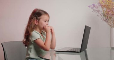 Çalışkan, sıkkın liseli kız, bilgisayar aracılığıyla öğretmeniyle video konferansında iletişim kurarak masada oturuyor. Küçük kız evde internetten eğitim görüyor.