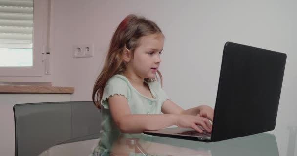 重点小女孩类型消息在笔记本电脑上的白色背景 可爱的学童坐在桌旁 按键盘上的按钮 — 图库视频影像