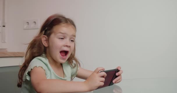 Маленька Дівчинка Грає Гру Смартфоні Екраном Хромакей Сидить Скляним Столом — стокове відео