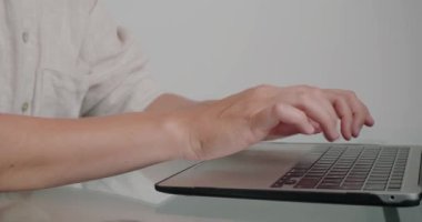 Ofisteki cam masada duran kadın tipleri dizüstü bilgisayardan rapor veriyor. Bayan çalışanın elleri modern cihazın klavyesindeki tuşlara basar.