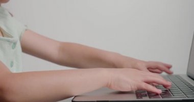 Küçük kızın elleri dizüstü bilgisayarın tuşlarına basıyor. Okul çocuğu evdeki modern elektronik cihazda masa başında yazı yazıyor.