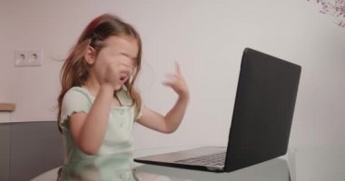 Komik kız klavyedeki tuşlara basarak mesaj yazmaya çalışıyor. Neşeli çocuk cam masada oturarak modern bir aletle yazmayı öğreniyor.