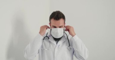 Erkek doktor yüzüne tıbbi maske takar ve kameraya bakar. Maskeli ve steteskoplu ciddi bir adam klinikte olağan çalışma gününe başlıyor.