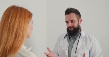 Erkek doktor klinikteki hastaya danışmanlık yapıyor. Beyaz önlüklü sakallı pratisyen, olgun kadınlara tavsiyelerde bulunur. İnsanın her zamanki çalışma günü.