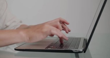 Bir kadının elleri klavyedeki tuşlara basıyor ve web sitesi için yeni bir makale yazıyor. Freelancer cam masada oturuyor ve uzaktan yakından çalışıyor.