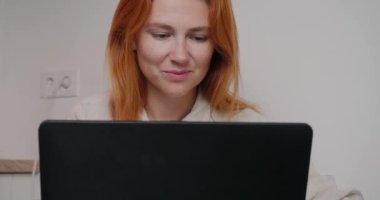 Tatmin olmuş bir kadın yeni bir proje üzerinde çalışıyor. Gülümseyen kızıl saçlı kadın ofis duvarının karşısında oturuyor.