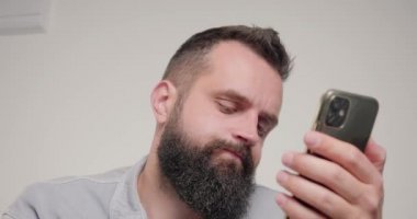 Sakallı adam akıllı telefondaki postaları kontrol etmek için gözlük takıyor. Genç çalışanlar işyerinde bej arka plan yakın plan cihazını kullanarak otururlar.