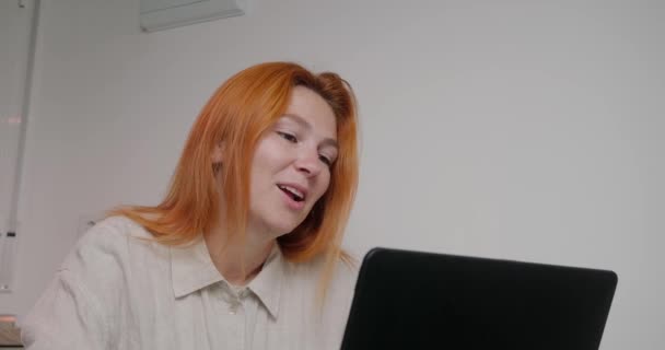 職場のガールフレンドと職場でのビデオ通話で話を終える赤毛の女性 女性従業員はノートパソコンを閉じて部屋を閉める — ストック動画