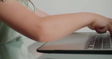 Okul çocuklarının parmakları beyaz arka plandaki cam masadaki modern cihazın klavye tuşlarına basıyor. Küçük kız dizüstü bilgisayarda mesajları yakın plan çekimde yazıyor.