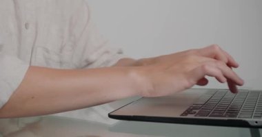 Bir kadının elleri klavyedeki tuşlara basıyor ve web sitesi için yeni bir makale yazıyor. Freelancer cam masada oturuyor ve uzaktan yakından çalışıyor.