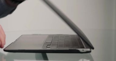 Tanınmayan adam dizüstü bilgisayarı cam masaya koyar ve projeyi yöneticiye göndermek için açar. Bir adamın elleri cihazın klavyesindeki düğmelere basar.