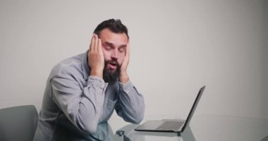 Freelancer ellerini başının üstüne koymaktan şikayetçi. Tereddütlü sakallı adam masada oturuyor ve bilgisayarını uzaktan kontrol ediyor.