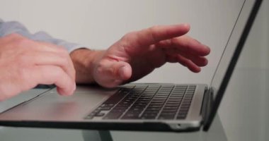 Programmer writes code for website using laptop in office. Hands of man press buttons of keyboard of electronic device on glass desk closeup