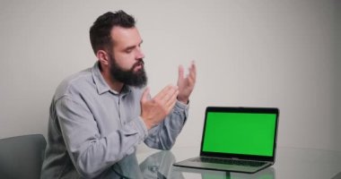 Profesyonel koç, dizüstü bilgisayardaki kromakey yeşil ekranda örnekler gösteren kod yazmaktan bahsediyor. Sakallı adam ofiste online video kursu yönetiyor.